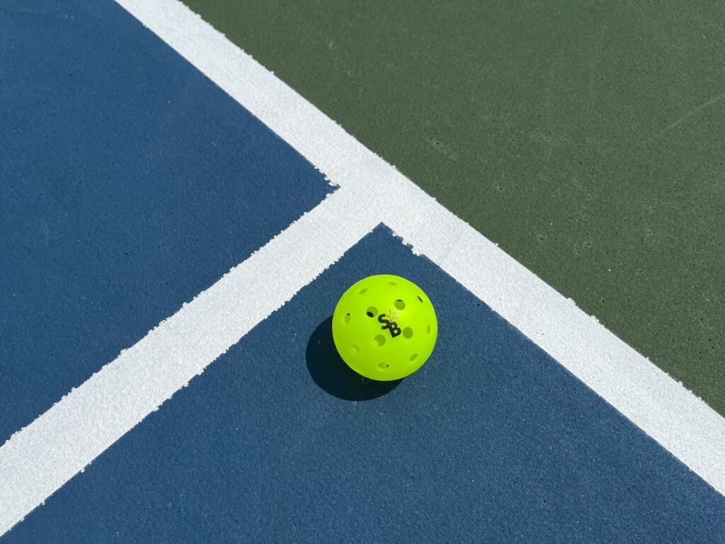 Bright yellow pickleball resting on a blue and green court, symbolising the growing interest in pickleball betting in Malaysia.